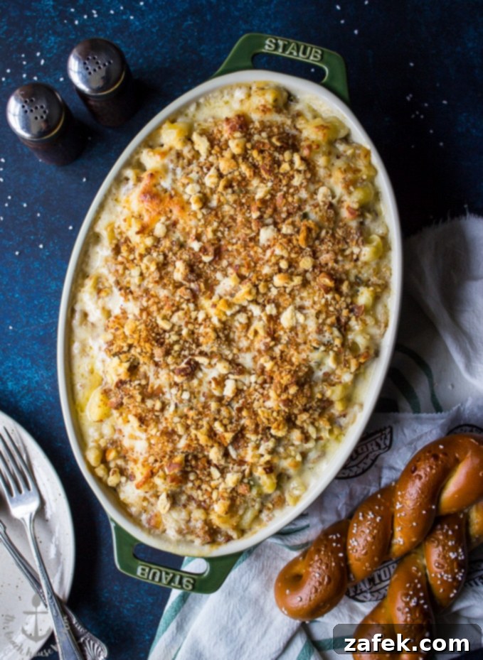 An overhead shot of Philly Cheesesteak Macaroni and Cheese, garnished and ready to serve, with the fuzzy background of soft pretzels.