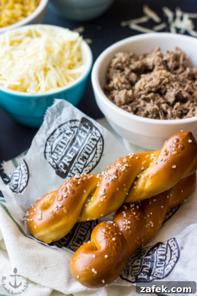 A composition featuring two iconic Philly soft pretzels alongside bowls of shredded cheese and cooked, thinly sliced steak meat, highlighting key ingredients for the mac and cheese.