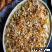 Overhead photo of Philly Cheesesteak Macaroni and Cheese in an oval dish with two hot pretzels in the background.