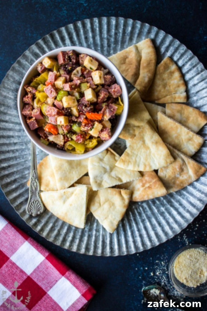Muffuletta Dip ina white bowl surrounded by pita wedges on a silver tray.