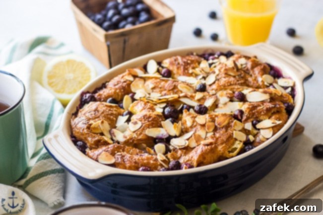 Blueberry Croissant Bread Pudding with Blueberry Sauce Blueberry Croissant Bread Pudding in a rustic blue oval dish, with fresh blueberries and a glass of orange juice in the soft background.