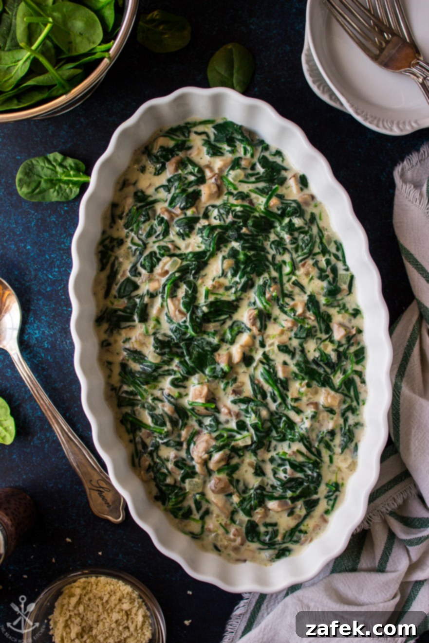 Overhead photo of Creamed Spinach and Mushrooms in an oval white dish, garnished lightly with fresh herbs