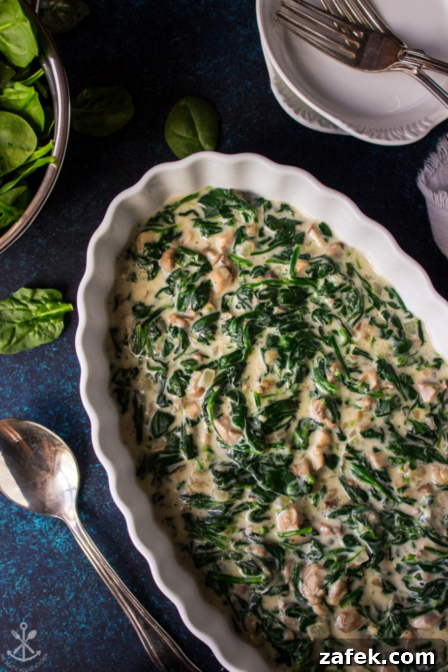 Up close photo of an oval dish of creamed spinach, highlighting the creamy texture and mushroom pieces