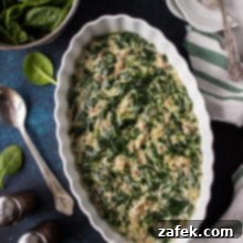 Overhead photo of Creamed Spinach in white oval dish on a blue background.