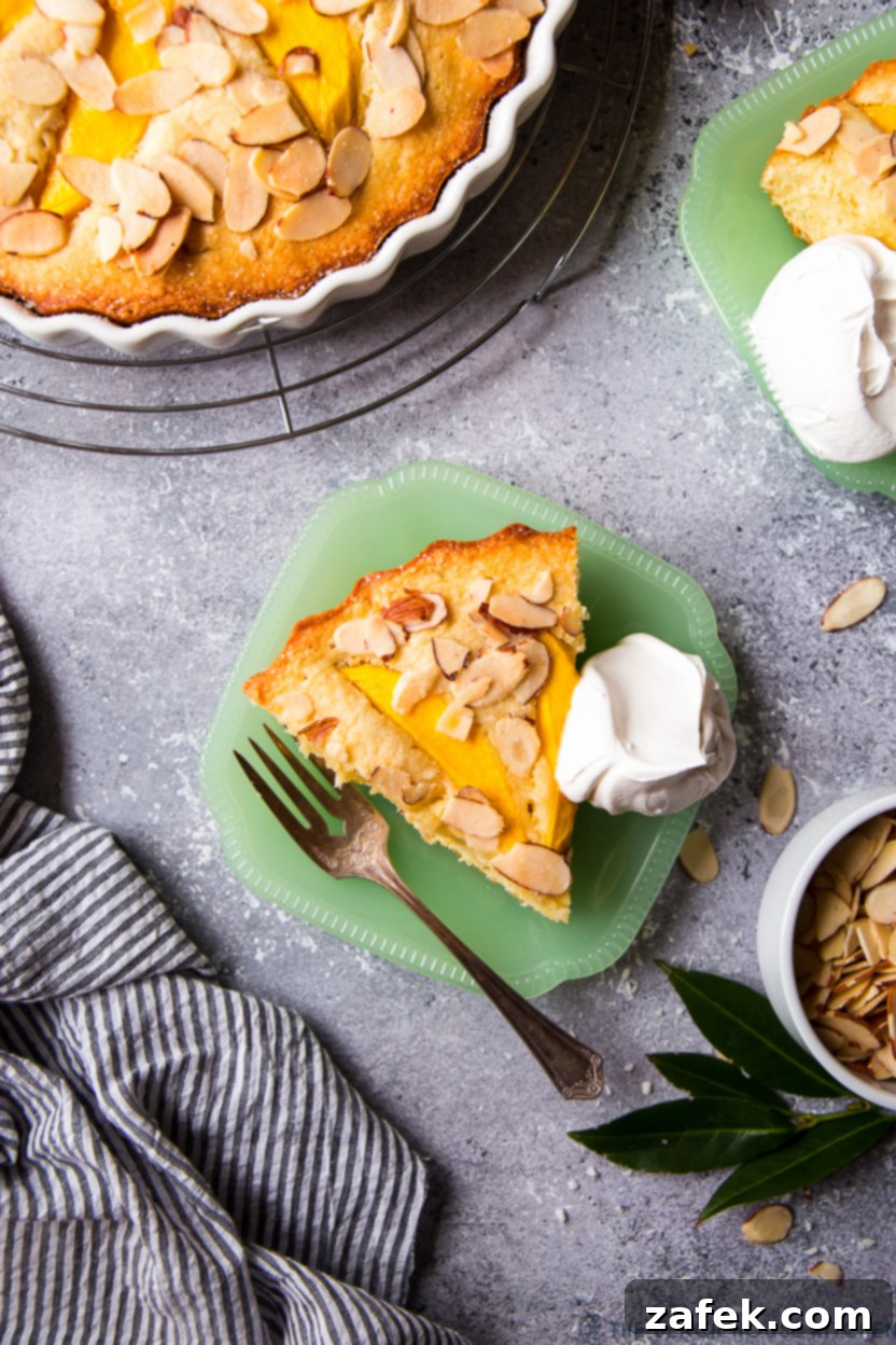 Overhead photo of a single slice of Tropical Mango Almond Cake served on a green plate, accompanied by a fork and a dollop of whipped cream.