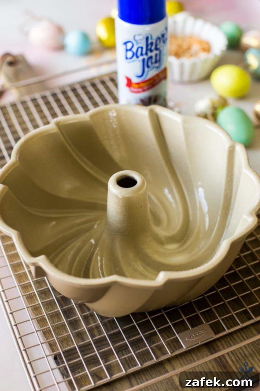 A greased swirled bundt pan on a wire rack with Easter eggs blurred in the background