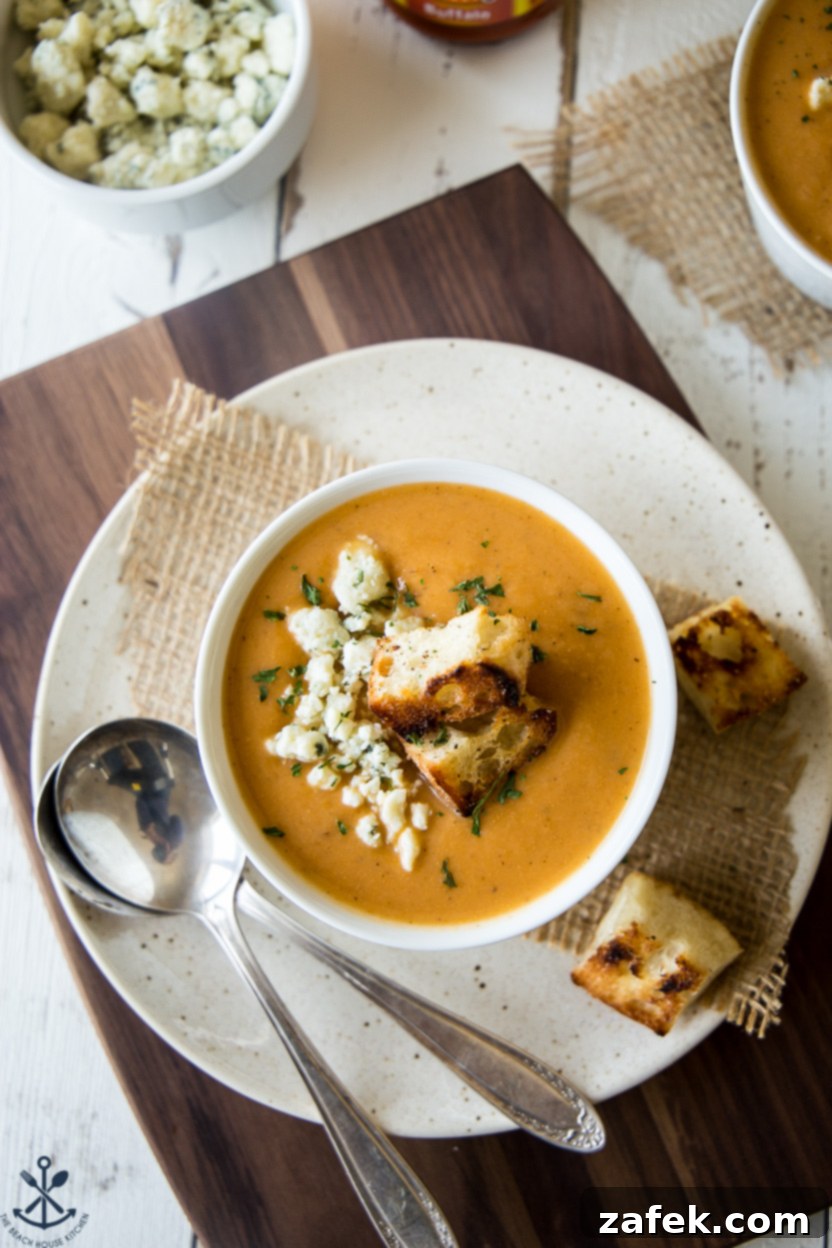 Overhead photo of a bowl of creamy Buffalo Cauliflower Soup garnished with fresh parsley and crunchy homemade croutons on a rustic wooden surface