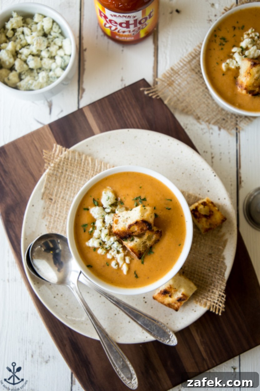 Close-up of a bowl of buffalo cauliflower soup topped with golden croutons, placed on a white plate with a fork, ready to be enjoyed