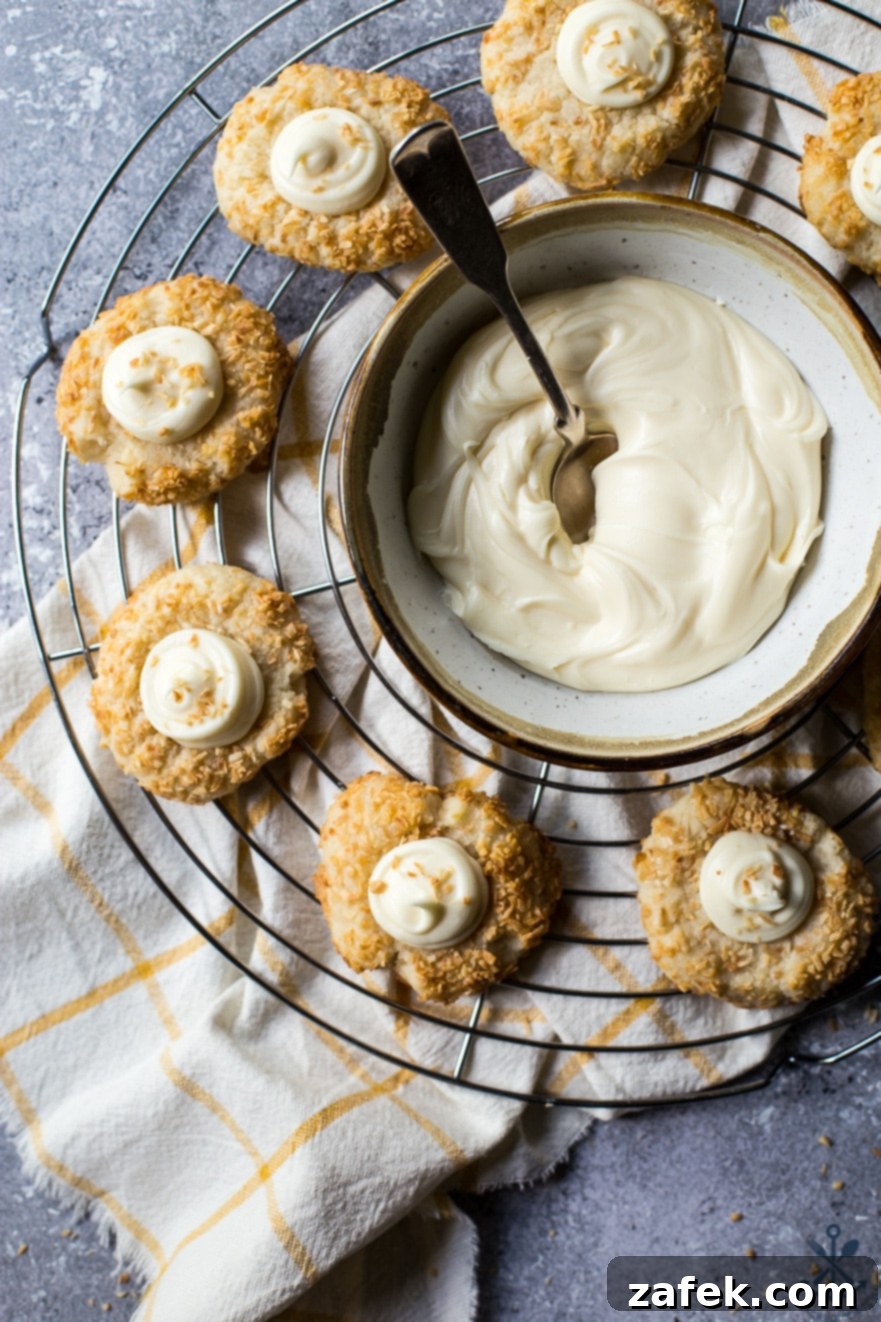Creamy Coconut Thumbprint Bites 2 Overhead photo of baking rack with coconut thumbprint cookies and a bowl of cream cheese frosting with a spoon