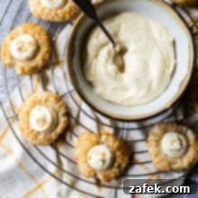 Creamy Coconut Thumbprint Bites 8 Overhead photo of round baking rack with coconut thumbprint cookies and a bowl of cream cheese frosting with a spoon