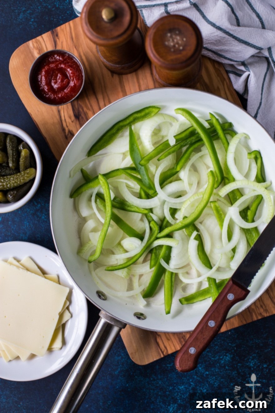 Philly French Dip Sandwich with Au Jus A close-up shot of a completed Philly French Dip Sandwich, showing the layers of beef, peppers, onions, and melted cheese, with a bowl of au jus for dipping.