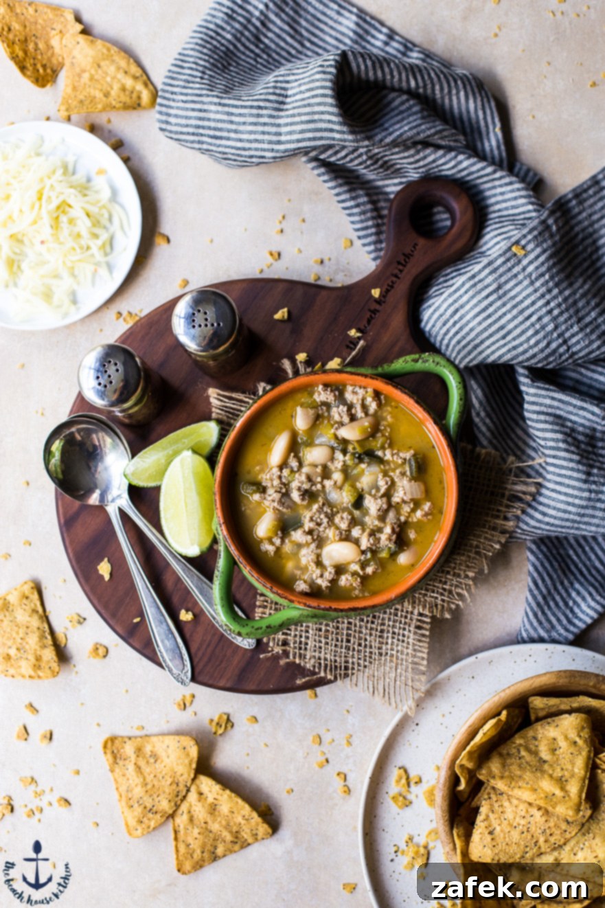 A small bowl of White Bean Turkey Chili on a wooden board with spoons, limes and tortilla chips