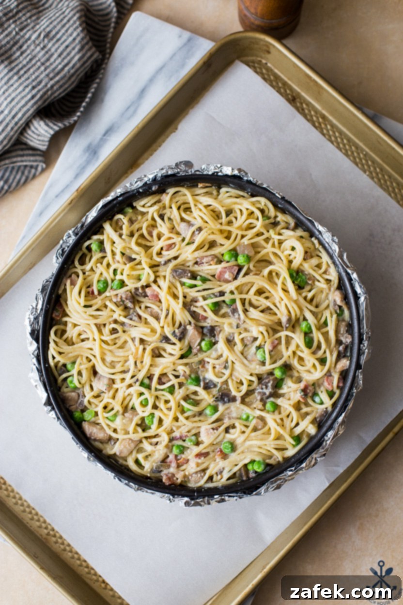Hearty Pancetta, Mushroom & Pea Spaghetti Pie 6 Overhead photo of a pre-baked spaghetti pie, generously topped with cheese, resting on a baking sheet before going into the oven