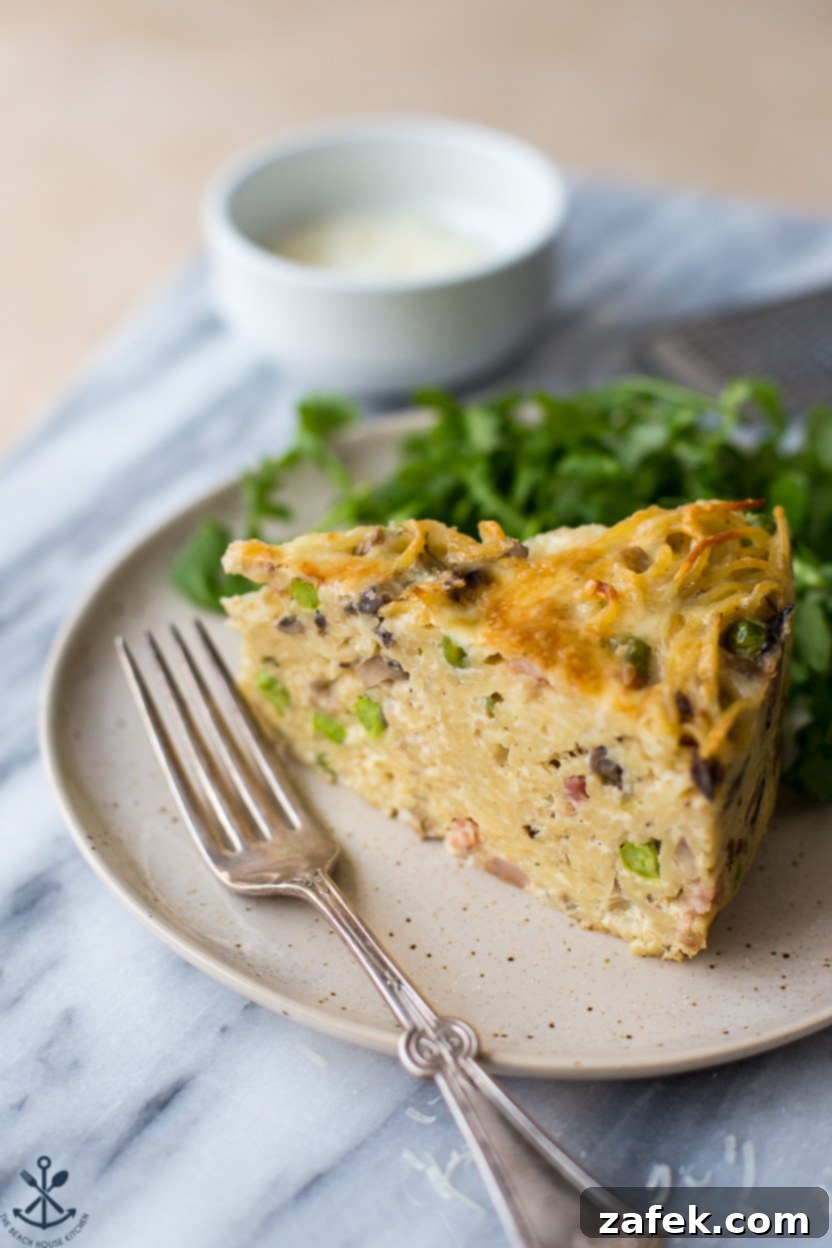 Hearty Pancetta, Mushroom & Pea Spaghetti Pie 7 A perfectly sliced wedge of spaghetti pie on a white plate, accompanied by a fork and fresh greens for garnish