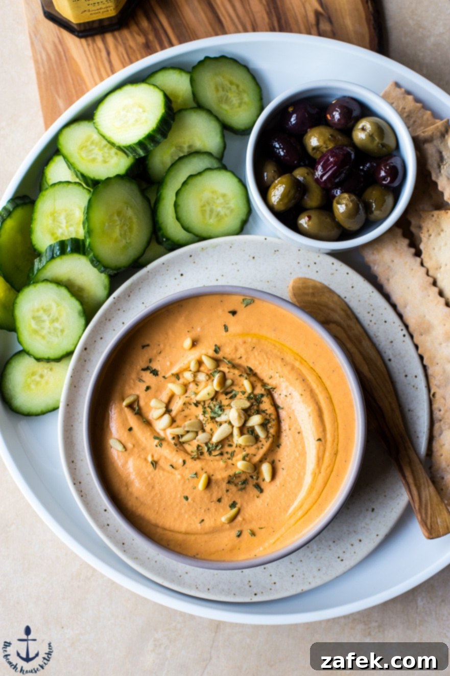 Assortment of fresh vegetables and crackers surrounding a bowl of White Bean Roasted Red Pepper Hummus.