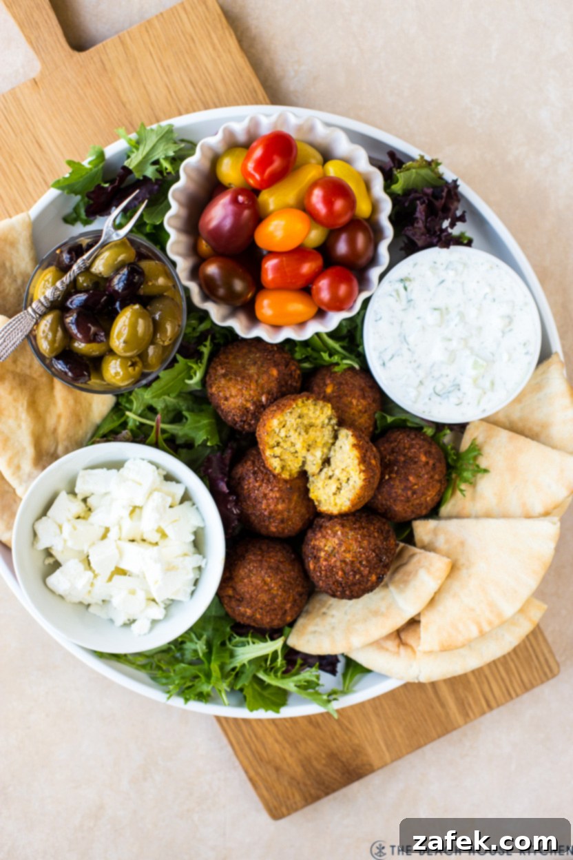 Overhead photo of a falafel platter with tzatziki sauce, tomatoes, feta, pita and olives
