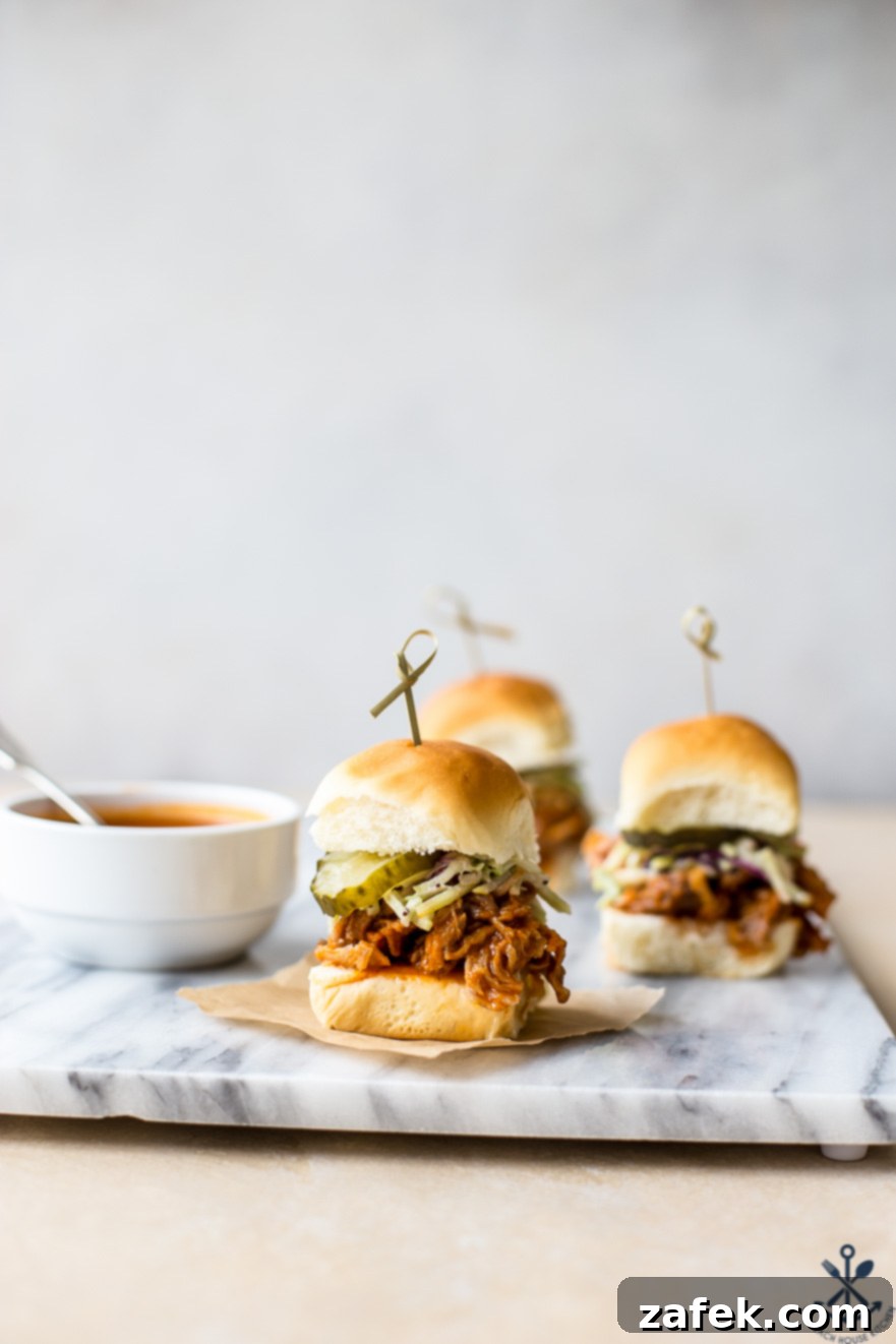 Sticky Sweet Heat Chicken Sliders 2 Hot honey pulled chicken sliders on a marble board, garnished with cilantro and served with a side of coleslaw and pickles