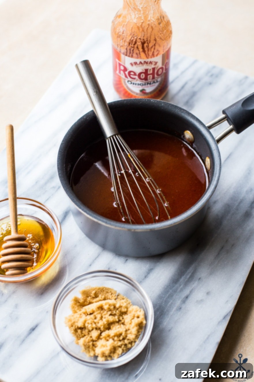 Sticky Sweet Heat Chicken Sliders 4 Close-up of key ingredients for hot honey pulled chicken sliders, including a bowl of rich honey, a bottle of hot sauce, and a dish of brown sugar and butter, displayed on a elegant marble board