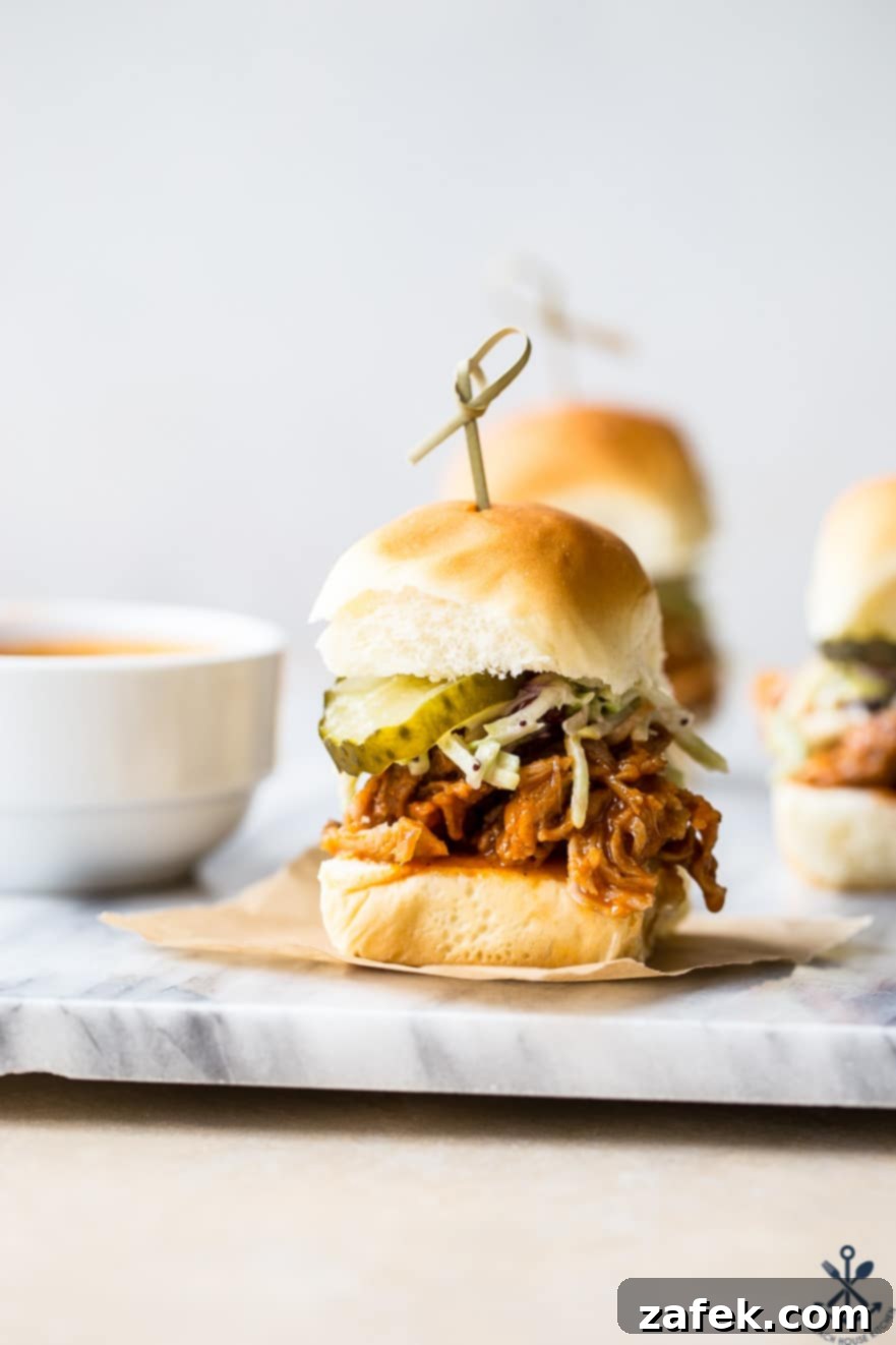 Sticky Sweet Heat Chicken Sliders 5 Beautifully arranged Hot Honey Pulled Chicken Sliders on soft buns, garnished with fresh cilantro, served on a rustic marble board with extra sauce and fresh dill pickles