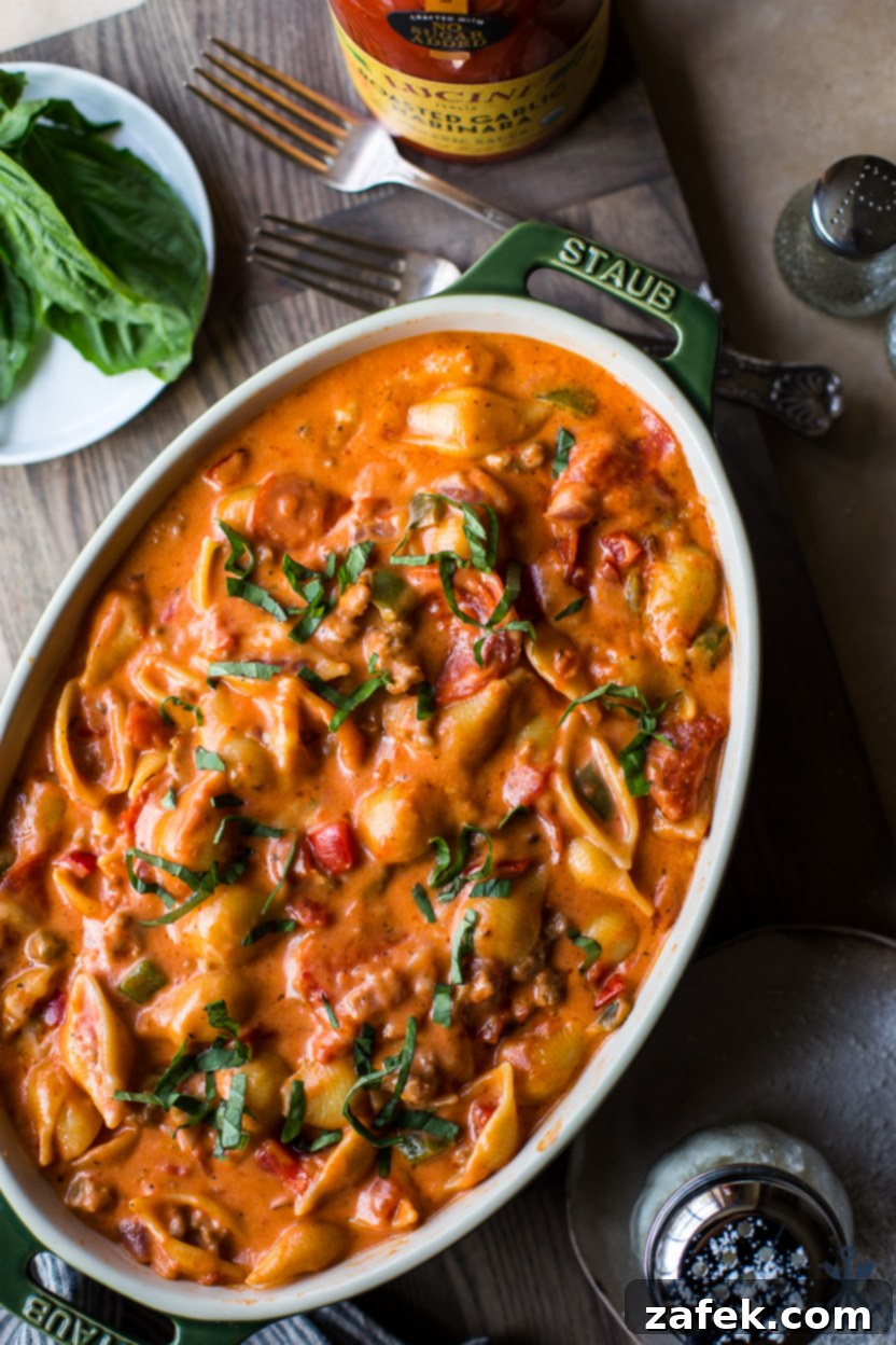 Up close overhead photo of a supreme pizza mac and cheese in an oval dish, with visible layers of pasta, cheese, and toppings