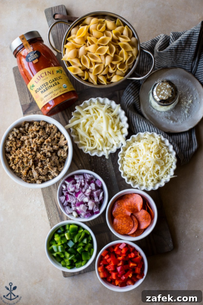 Overhead photo of individual ingredients for supreme pizza mac and cheese laid out, including pasta, sausage, bell peppers, onions, cheese, and marinara