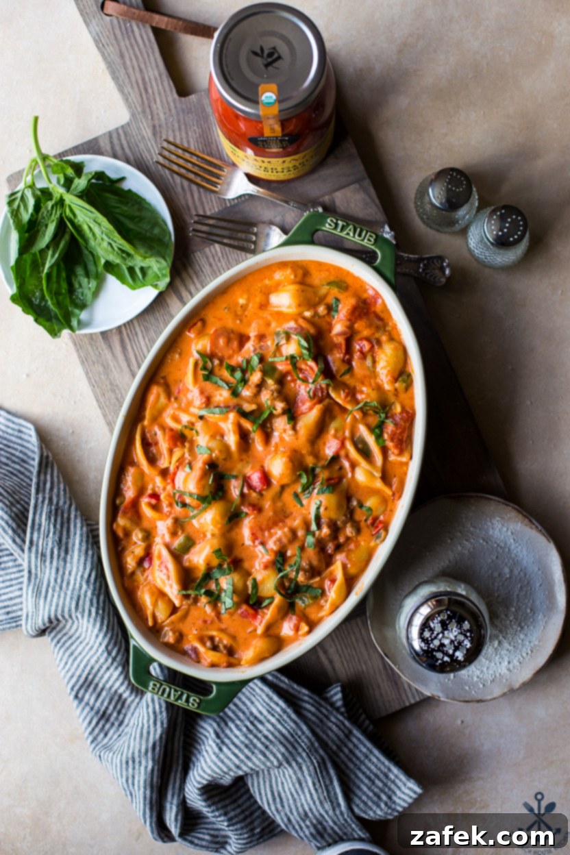 Overhead photo of an oval baking dish filled with a supreme pizza mac and cheese mixture before baking, topped with extra cheese and pepperoni