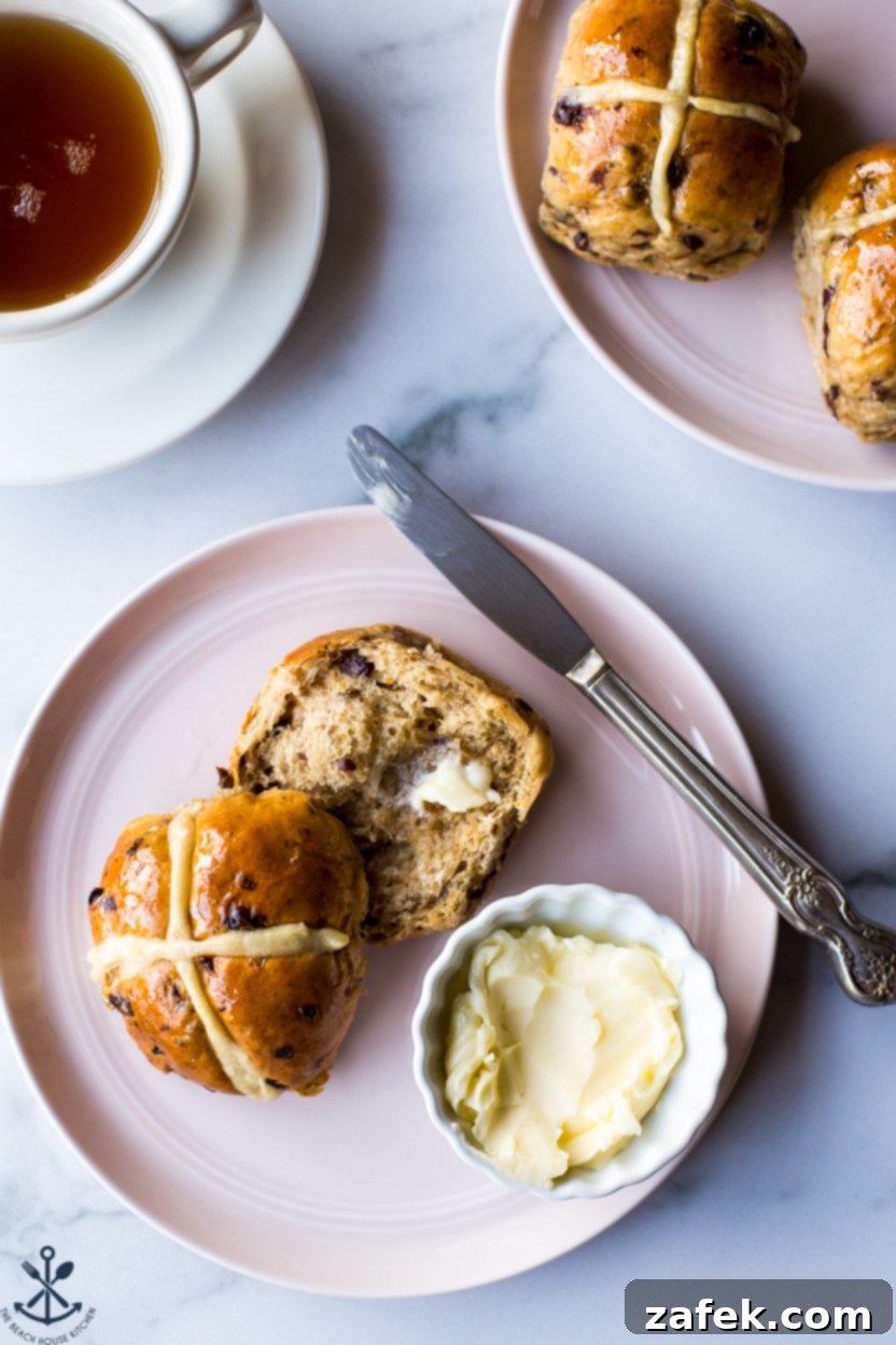 Spiced Easter Buns 2 Overhead photo of a perfectly baked Hot Cross Bun on a delicate pink plate with a pat of butter, inviting a first bite.