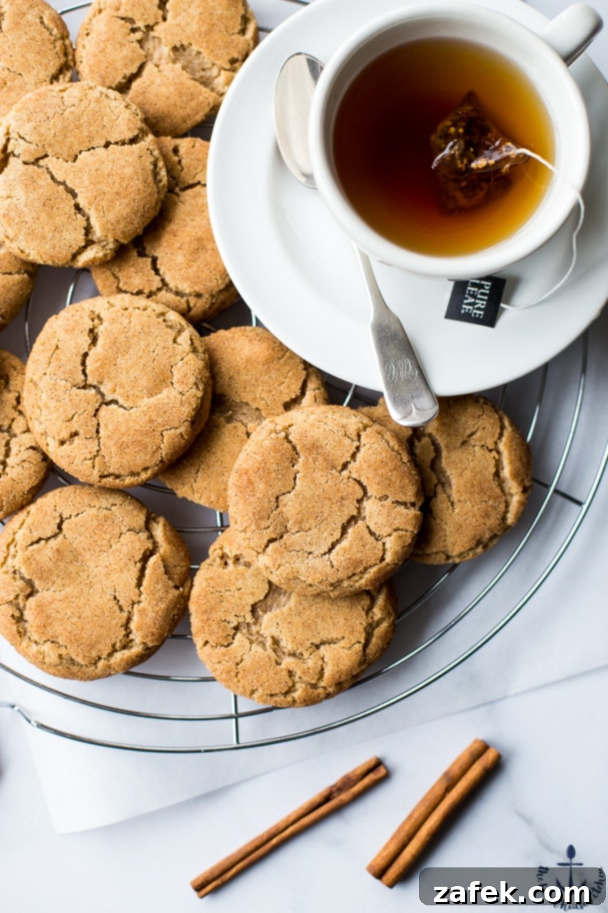 Warm Chai Spiced Snickerdoodle Cookies 3 A close-up view of Chai Snickerdoodle Cookies on a cooling rack, perfectly showcasing their crinkled, sugar-coated tops and soft centers, with a blurred teacup in the background.