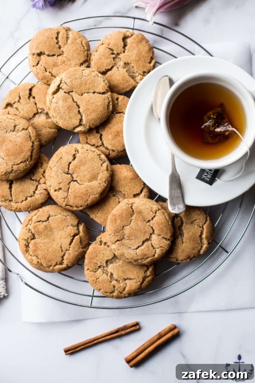 Warm Chai Spiced Snickerdoodle Cookies 5 An overhead view of a batch of Chai Snickerdoodle Cookies on a wire cooling rack, accompanied by a cup of hot tea, inviting a moment of warmth and indulgence.