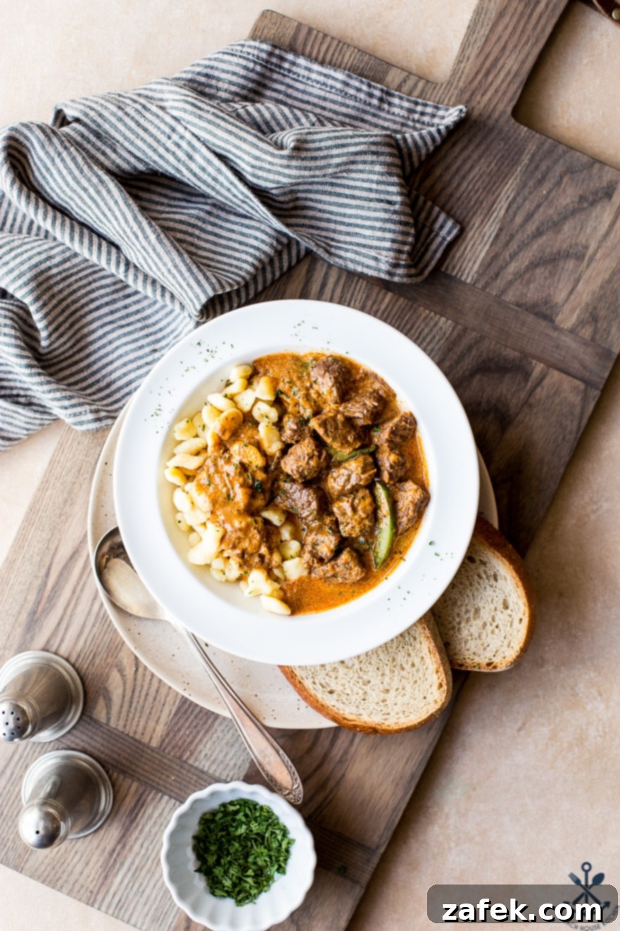 Overhead photo of Hungarian beef goulash in a white bowl on a wooden board, showcasing its rich color and tender beef