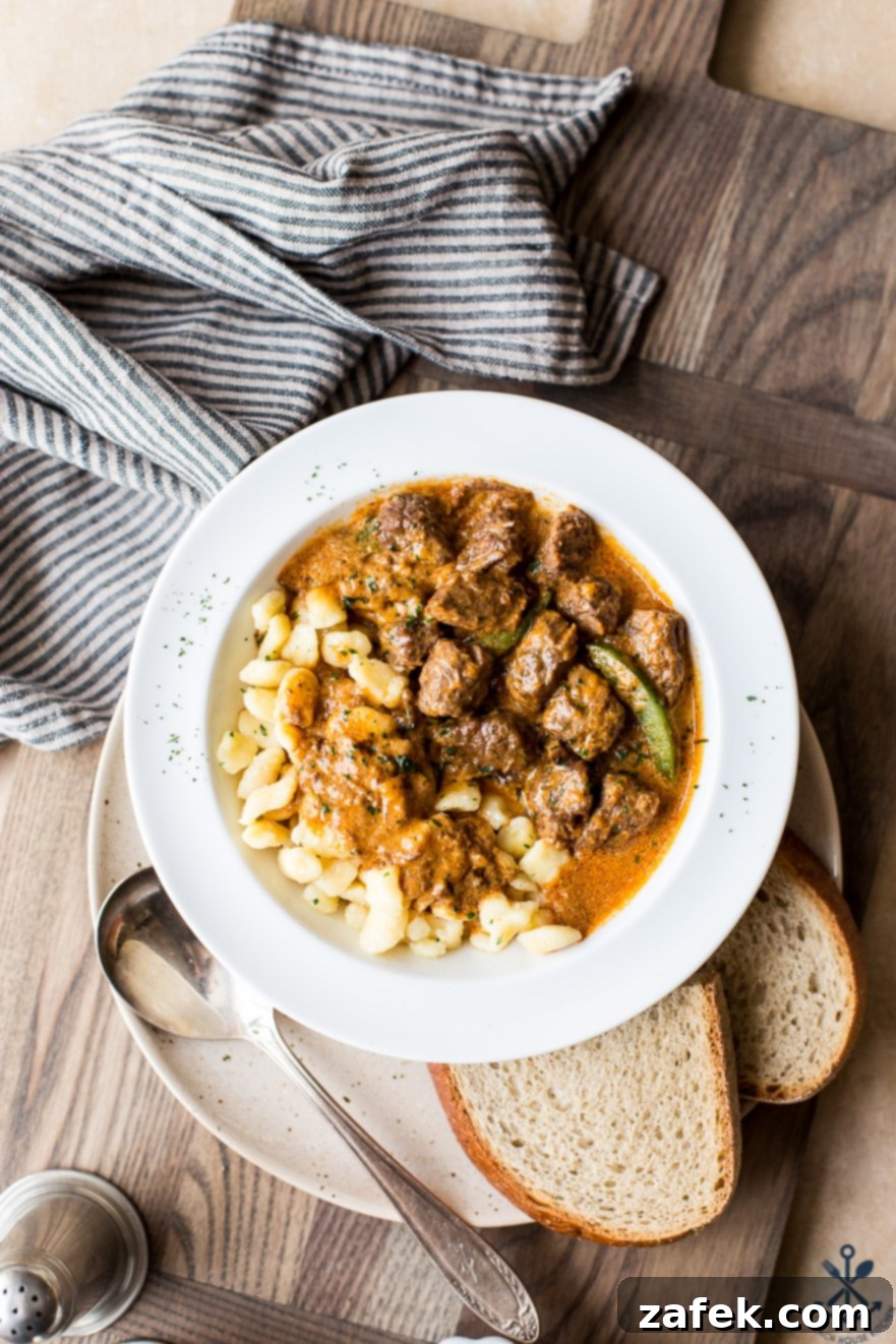 Overhead photo of Hungarian beef goulash in a white bowl on a wooden board, garnished with fresh parsley