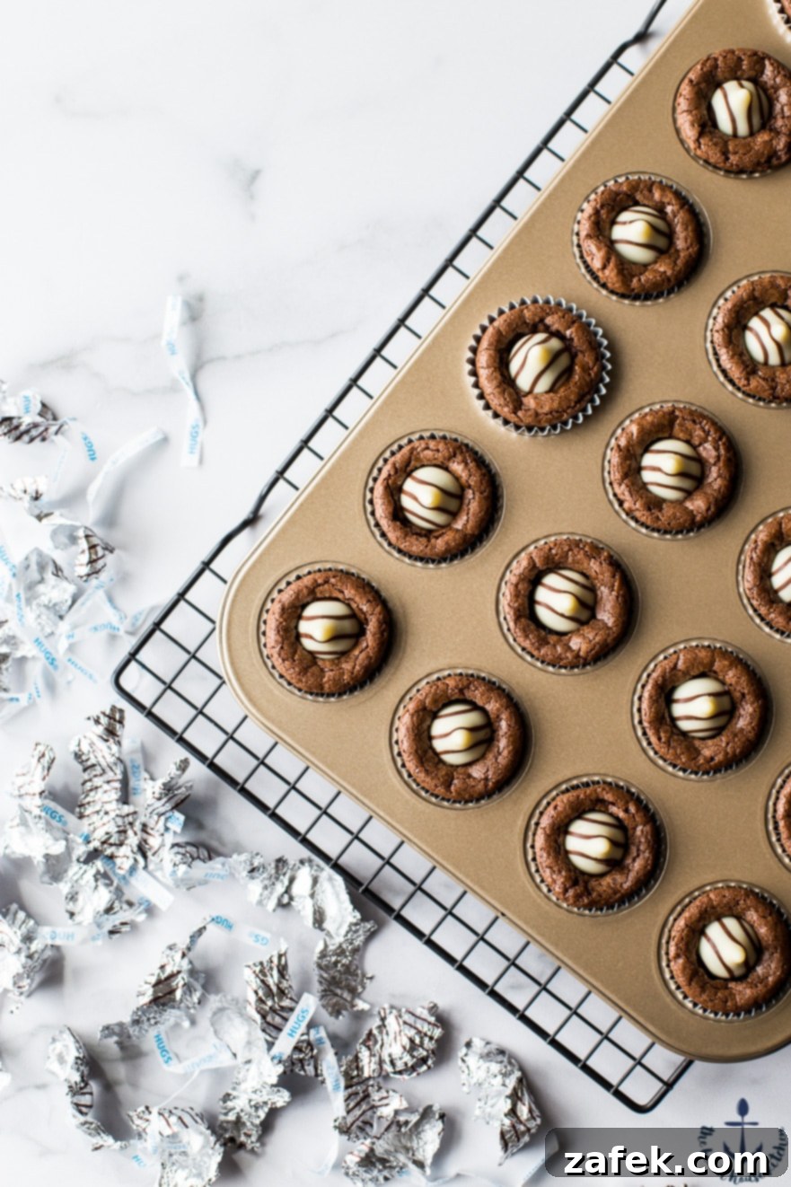 Hershey's Hug Brownie Bites Overhead photo of Hershey's Hug Brownie Bites in a gold muffin pan, with one brownie having a visible melted chocolate hug.