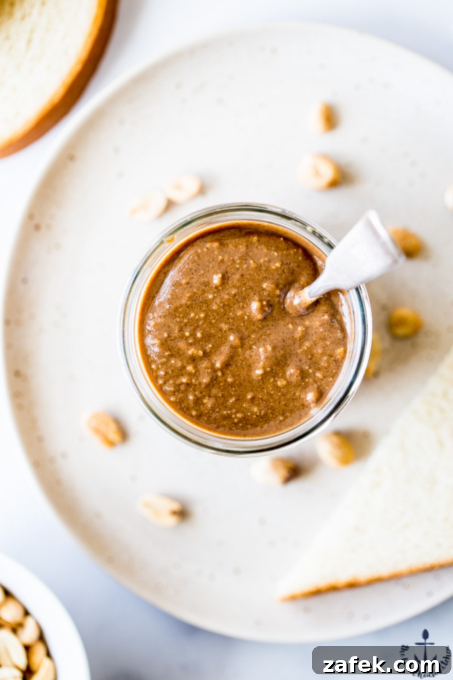 Barista Blend Peanut Butter 3 An overhead view of a perfectly crafted jar of Cappuccino Peanut Butter, a silver spoon nestled within, ready to be enjoyed with a rustic slice of bread.