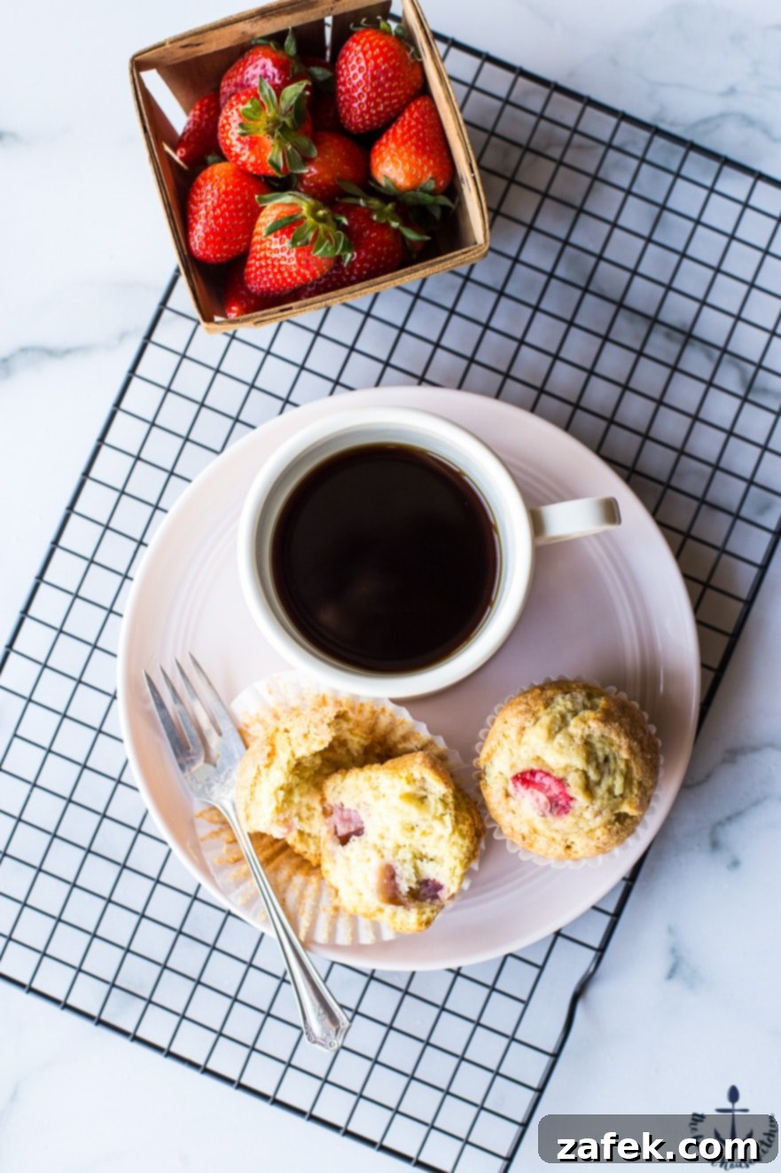 Sunshine Strawberry Lemon Muffins 2 Freshly baked strawberry lemon muffins on a plate, with a cup of coffee and a small crate of strawberries beside them, suggesting a delightful breakfast scene.