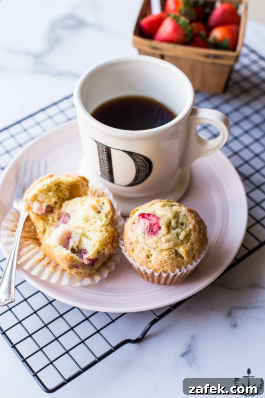 Sunshine Strawberry Lemon Muffins 5 Close-up of baked strawberry lemon muffins on a plate, highlighting their golden tops and the vibrant specks of strawberries, with a coffee cup in the background.