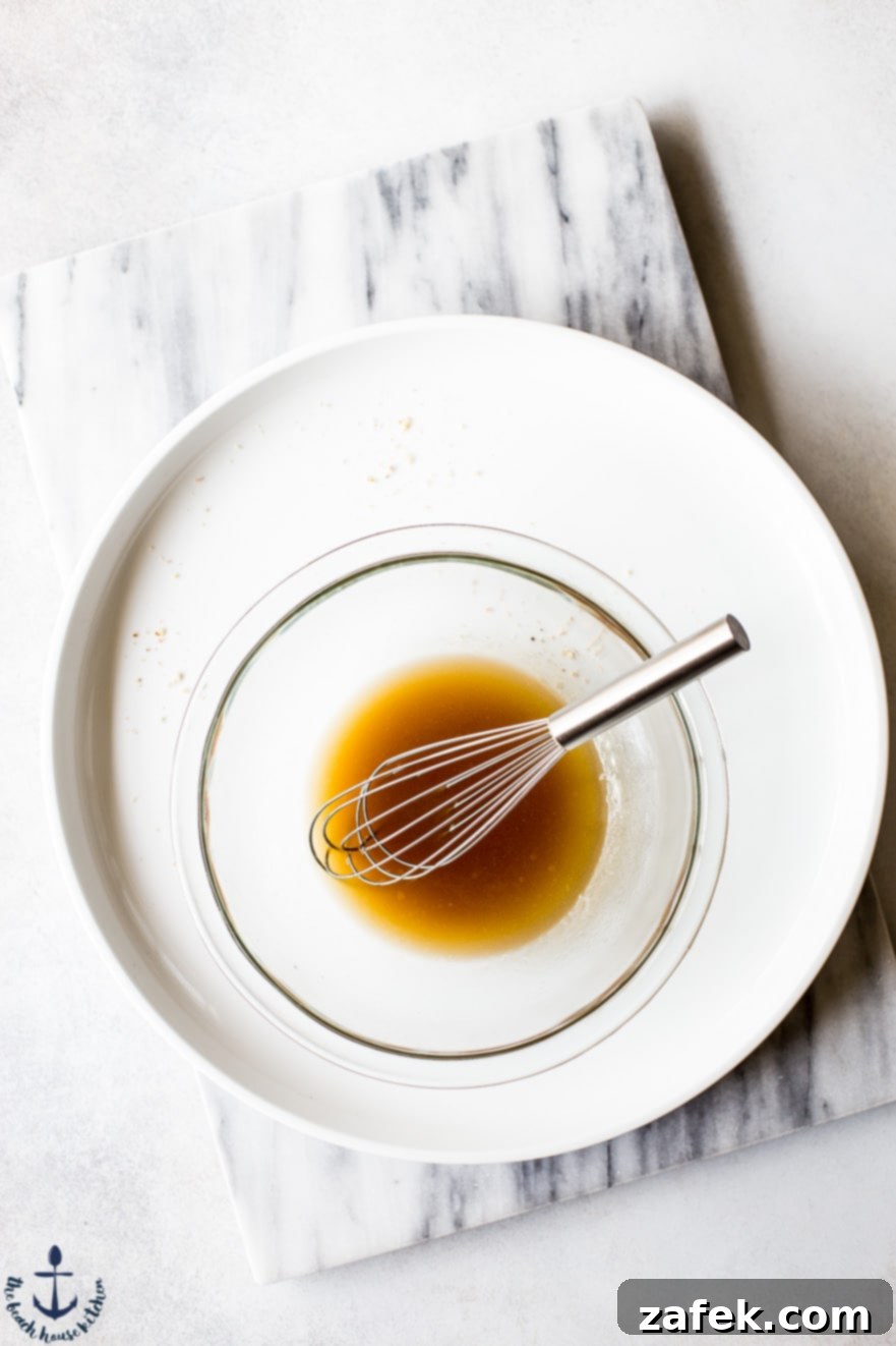 Overhead shot of a clear mixing bowl filled with golden maple syrup and a whisk, ready for combining ingredients for the breakfast bites.
