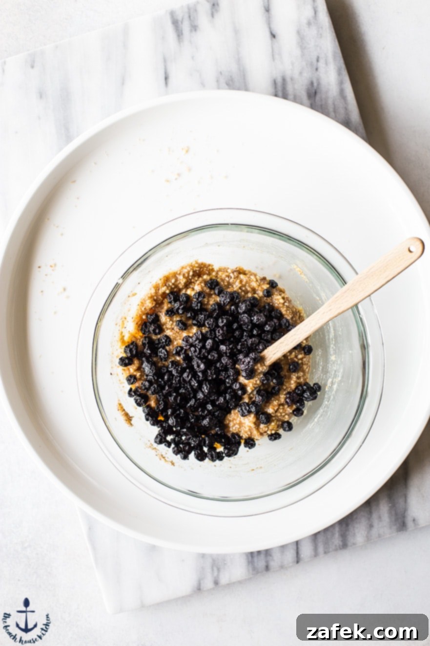 Close-up of the blueberry lemon breakfast bite dough in a clear bowl, with dried blueberries folded in, ready for shaping.