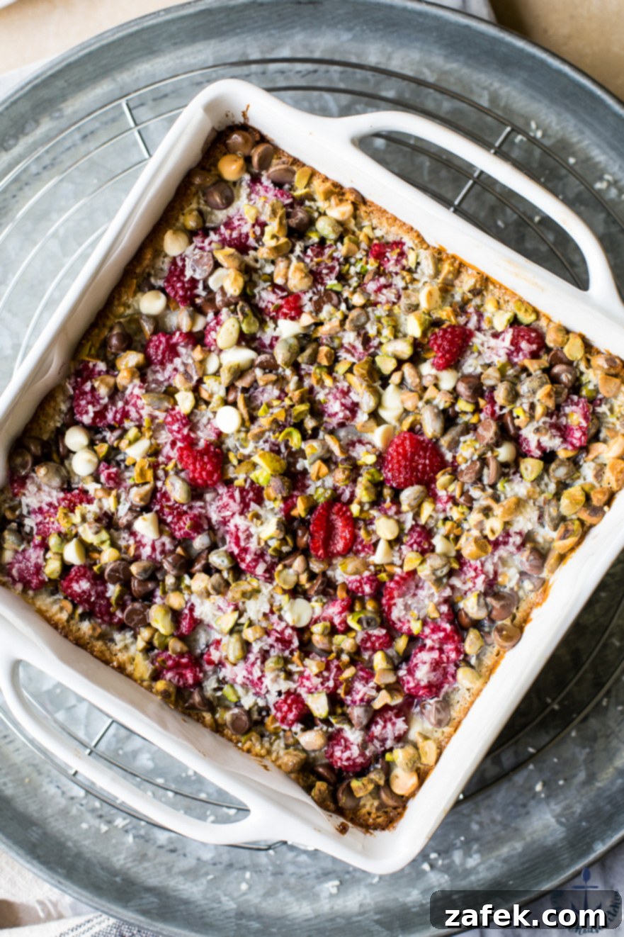 Overhead shot of freshly baked Raspberry Pistachio Magic Bars, perfectly cut into squares, showcasing the vibrant red raspberries and green pistachios against a backdrop of golden crust.