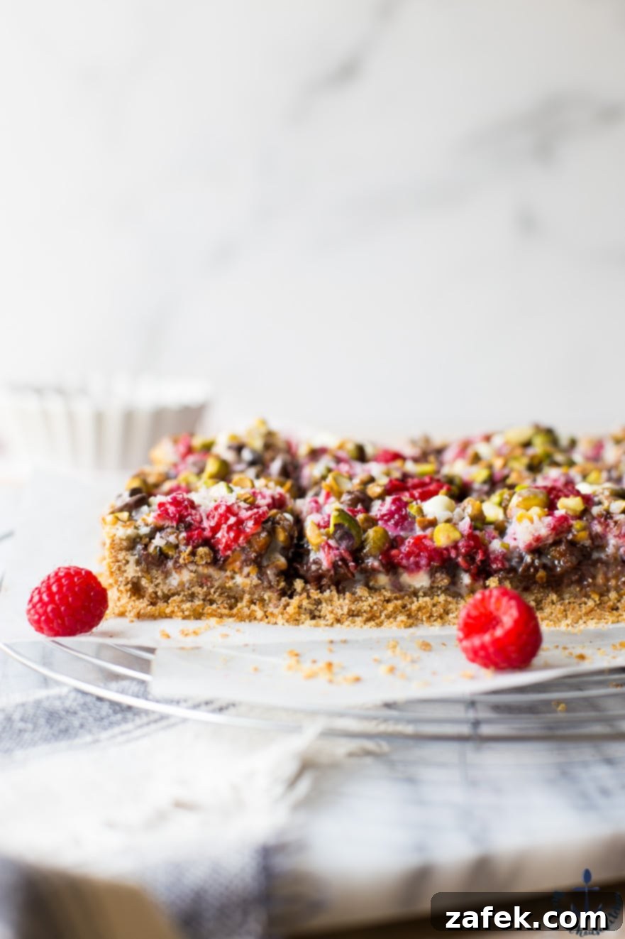 Close-up of two Raspberry Pistachio Magic Bars, adorned with fresh raspberries, highlighting the intricate layers and inviting textures.