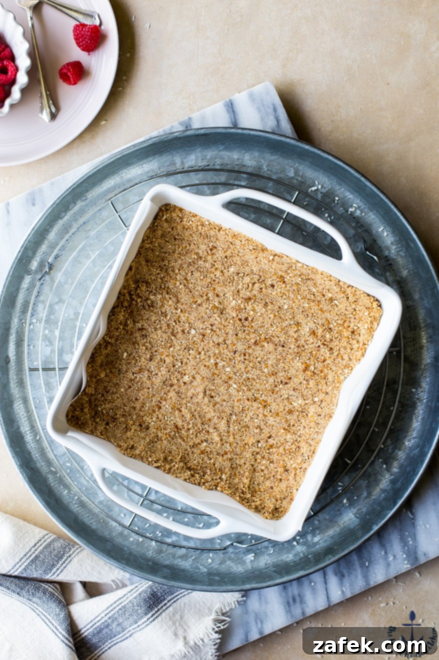 A perfectly pressed pretzel crust in a white baking pan, sitting on a silver tray, demonstrating the sturdy and inviting base for the magic bars.