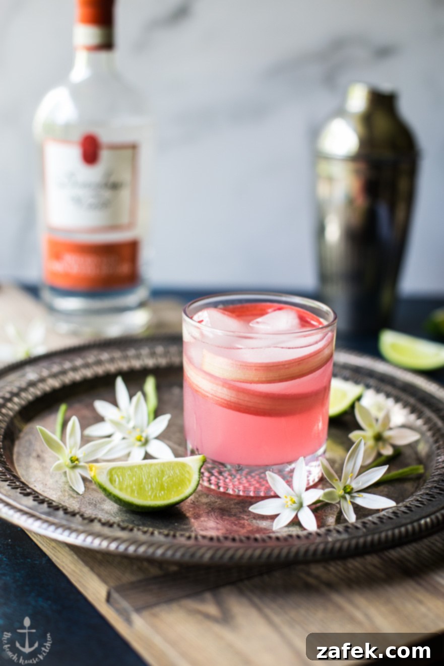 A stunning pink Spiced Rhubarb Collins cocktail, elegantly served on a silver tray, adorned with fresh flowers and lime slices, evoking a sense of celebration and spring.