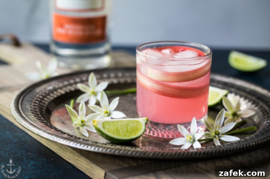 A close-up shot of the refreshing Spiced Rhubarb Collins cocktail, highlighting its beautiful pink color and delicate garnish, set against a backdrop of spring blooms.