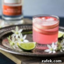 Photo of a pink spiced rhubarb collins cocktail on a silver tray surrounded by flowers and limes.