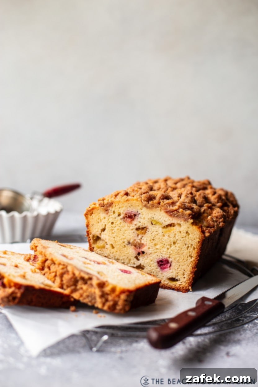 A rhubarb crumb loaf sliced on a round wire rack with a sharp knife