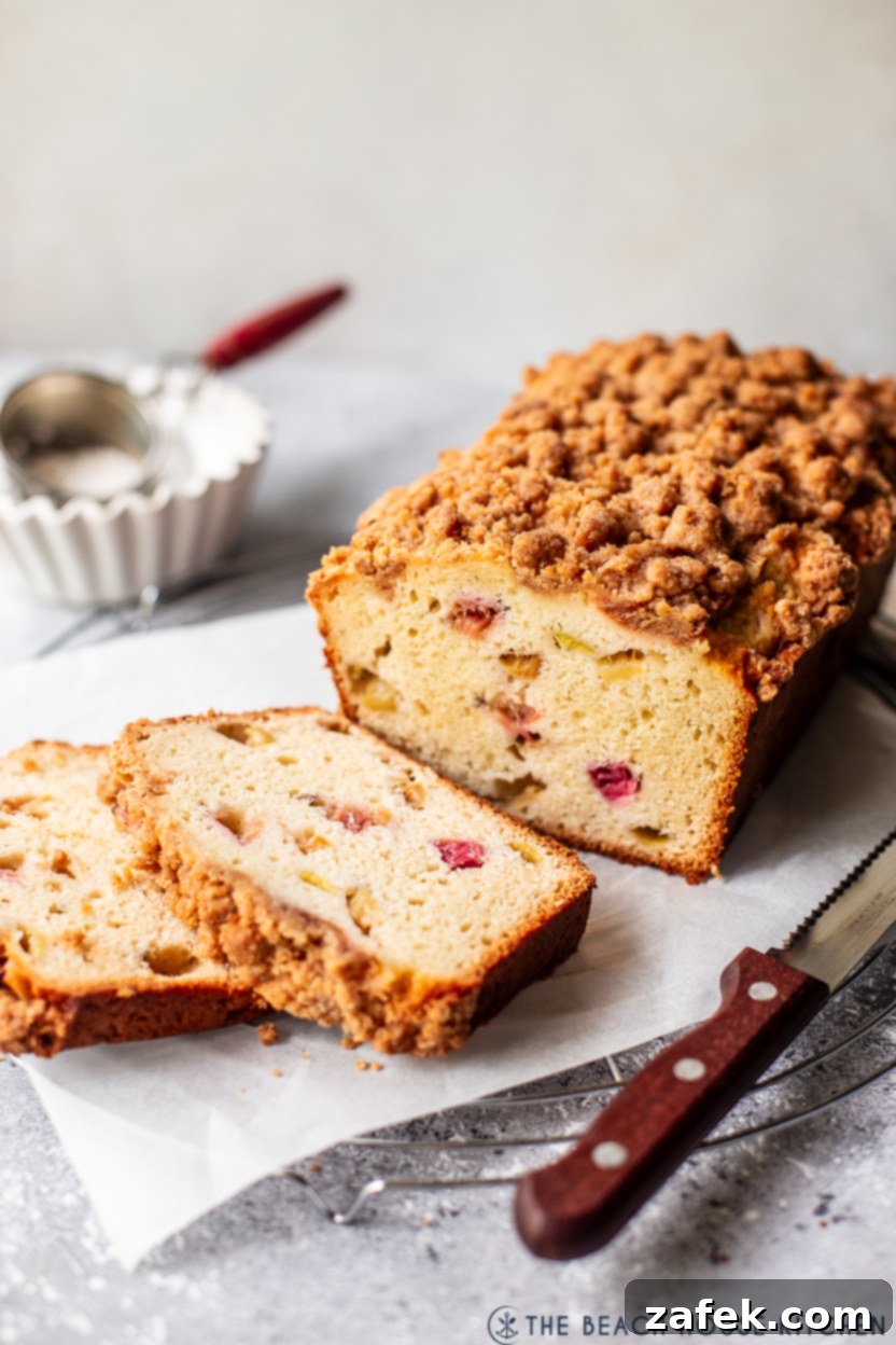 A sliced rhubarb crumb loaf on a round wire rack with a sharp knife