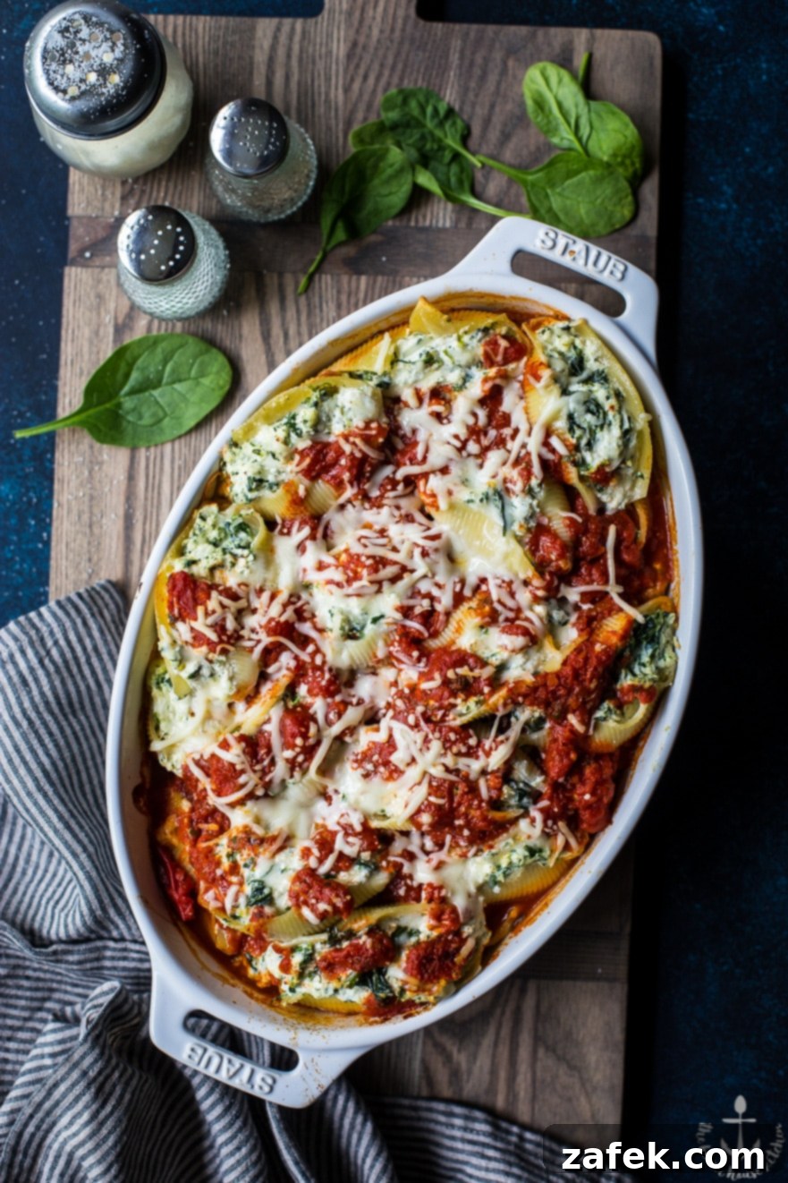Overhead photo of easy spinach stuffed shells in a white dish on a wooden board, garnished with fresh basil