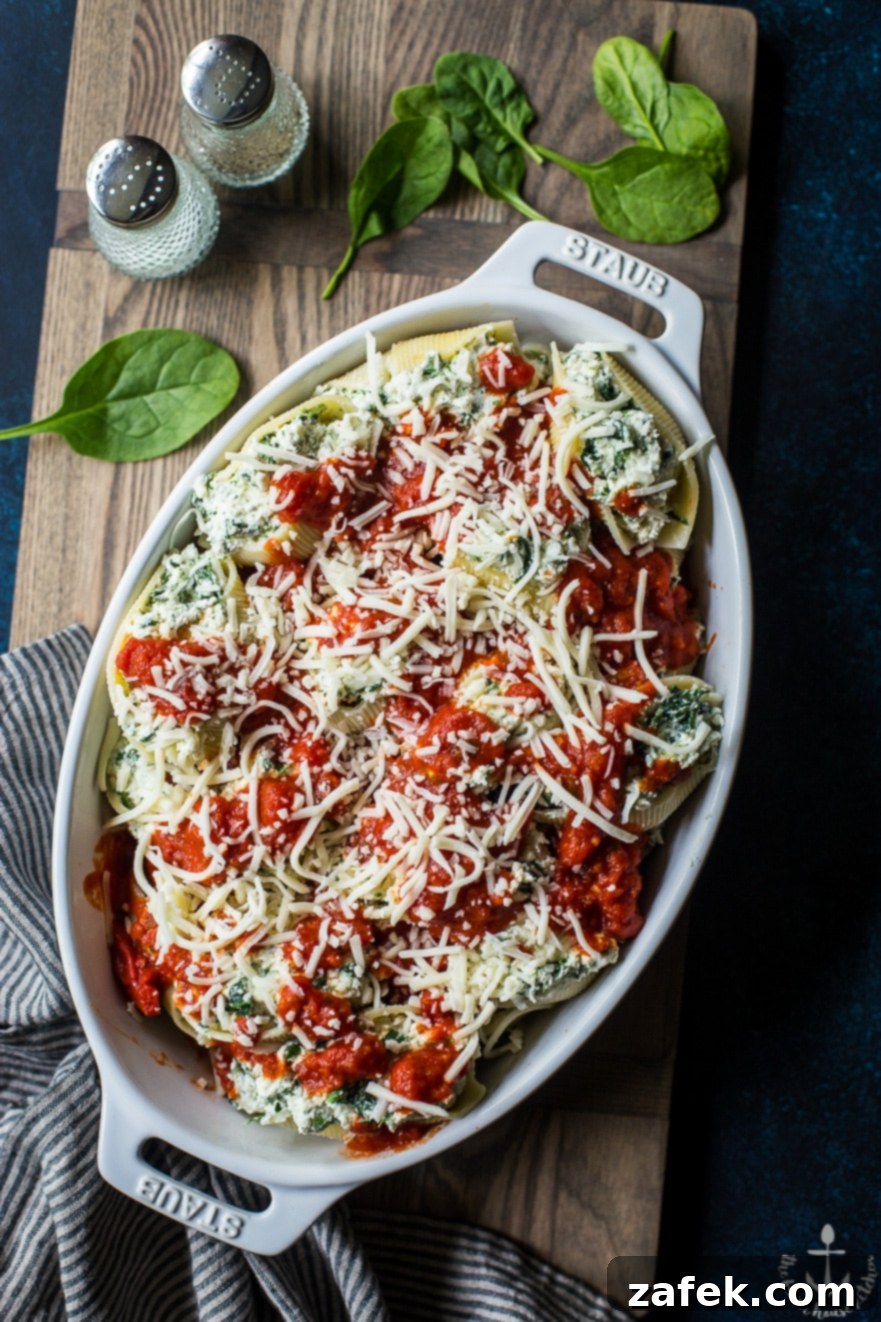 Overhead photo of precooked easy spinach stuffed shells in white dish on wooden board, ready for baking