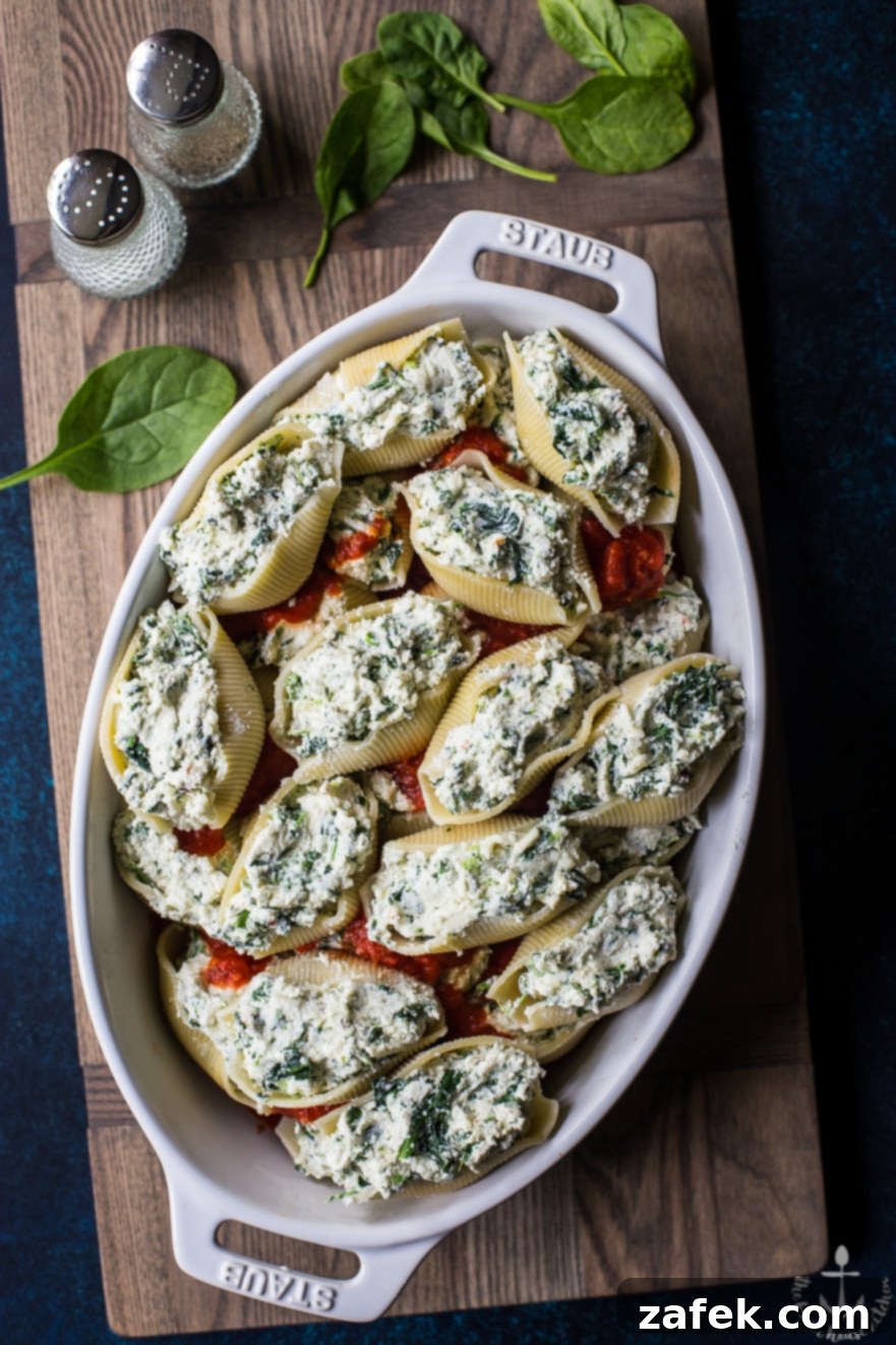 Precooked easy spinach stuffed shells in white dish on wooden board, with a focus on the cheesy topping