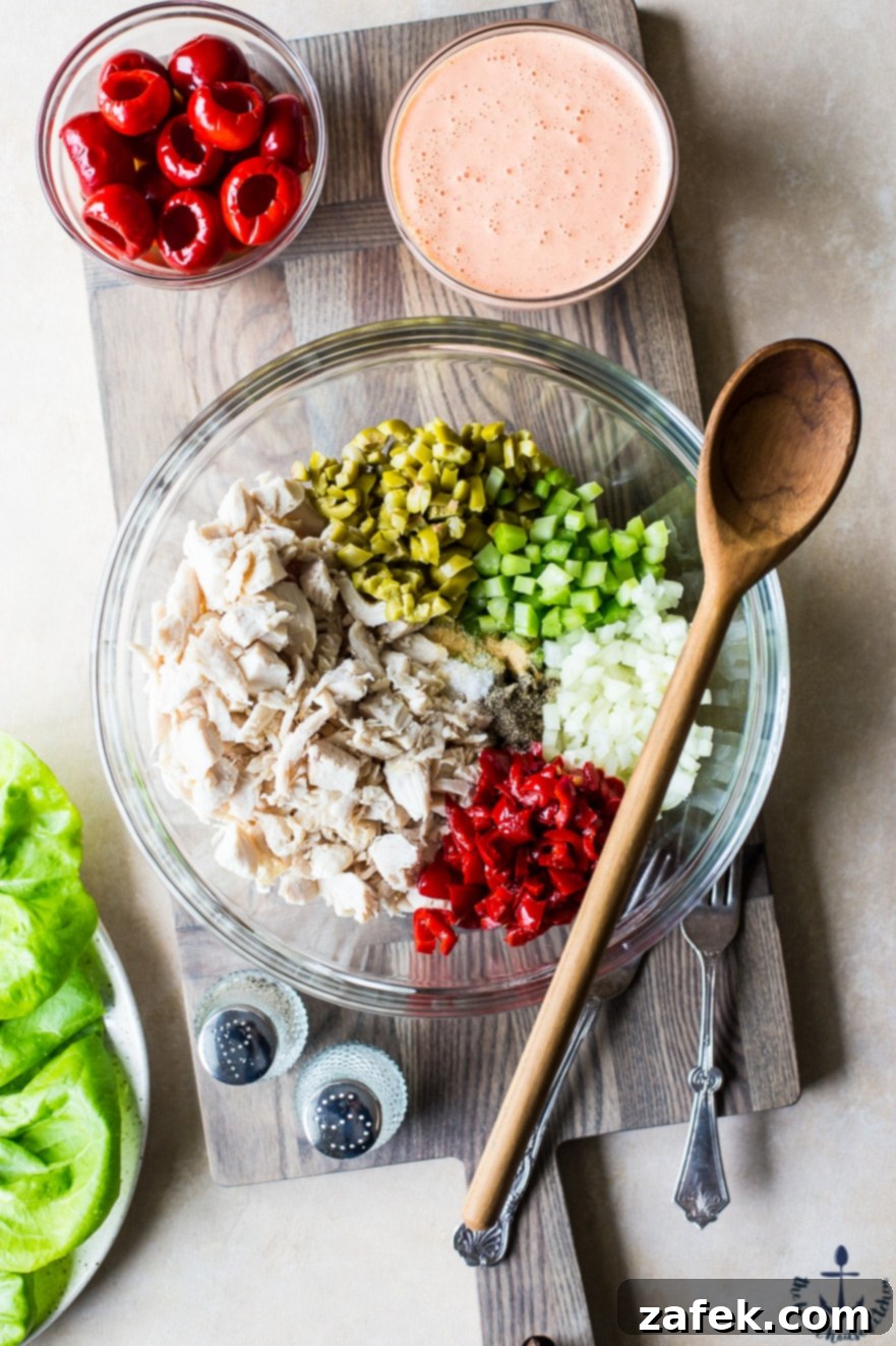 Mediterranean Peppadew and Olive Chicken Salad 6 Photo of ingredients for chicken salad with peppadews and olives in glass bowl with wooden spoon on top