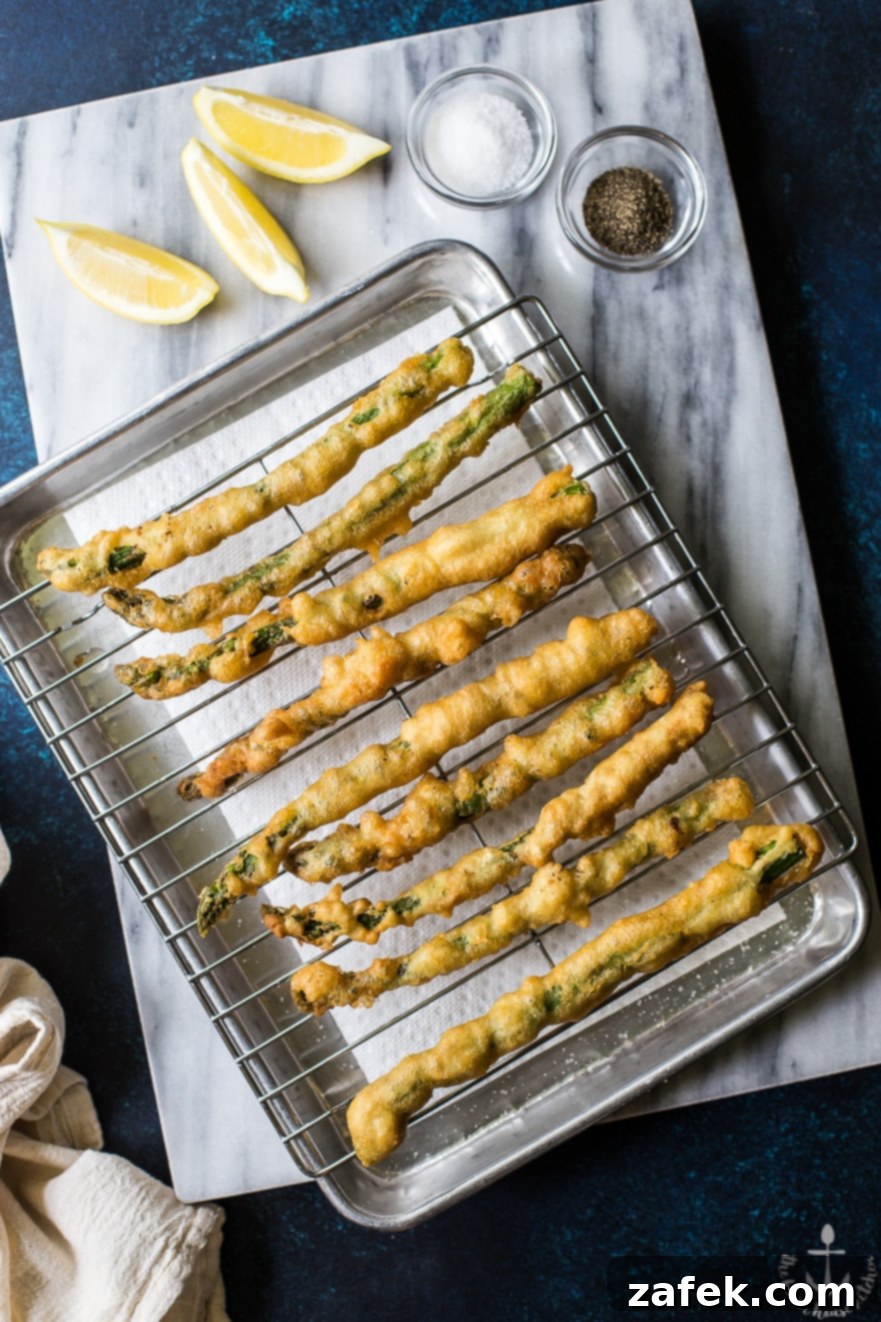 Overhead photo of asparagus tempura on a rack on a silver tray